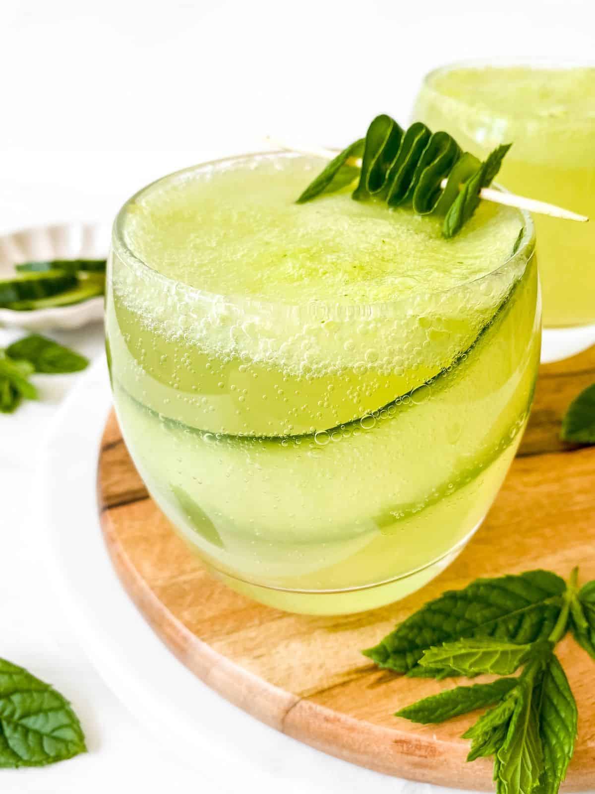 cucumber mint mocktail in a glass on a wooden board next to mint leaves.