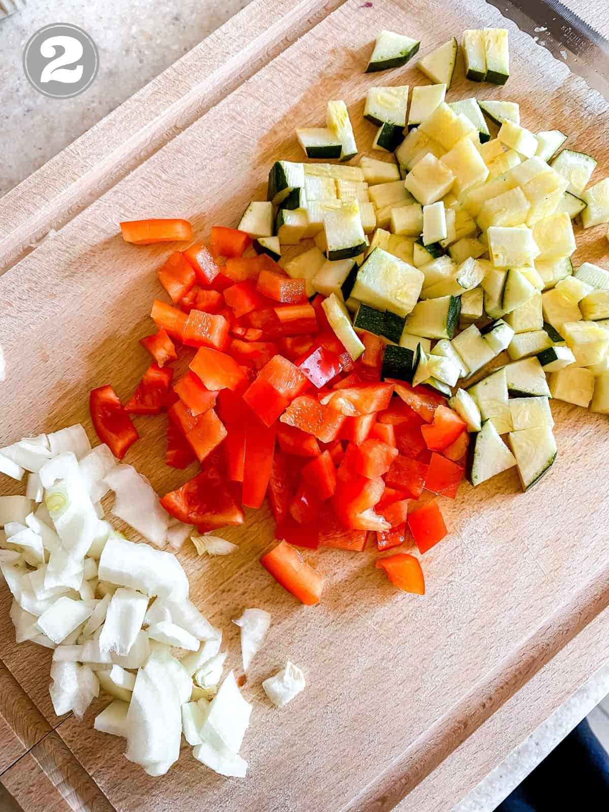 diced bell pepper, onion and zucchini on a wooden board.