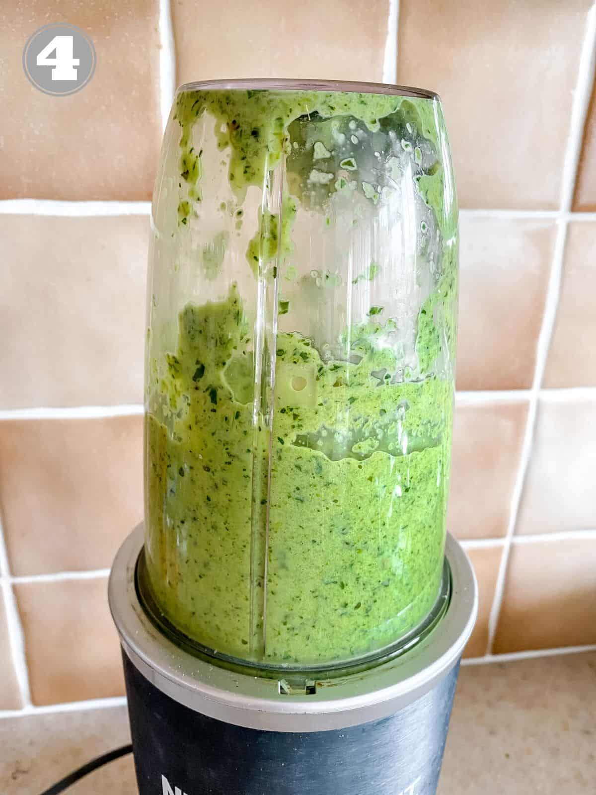 green pasta sauce in a blender in front of a brown tiled wall.