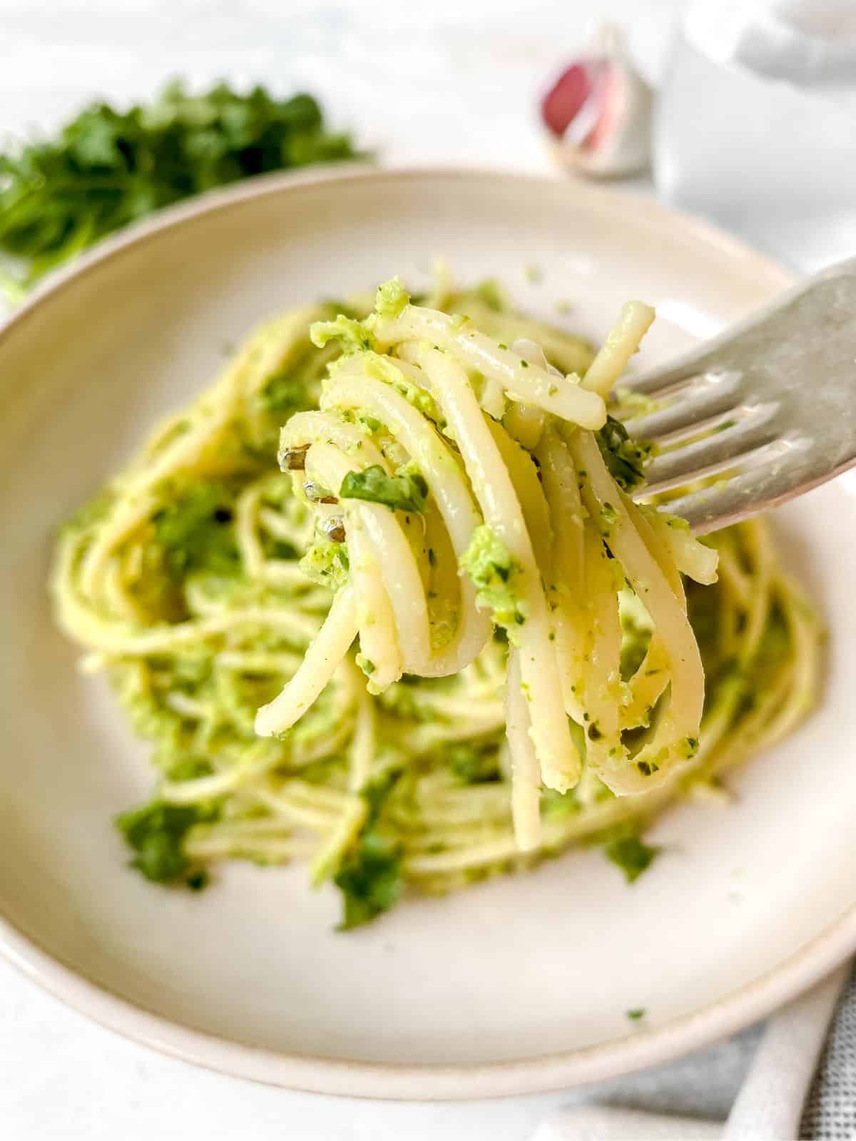 fork holding spaghetti with green sauce above a light brown bowl.