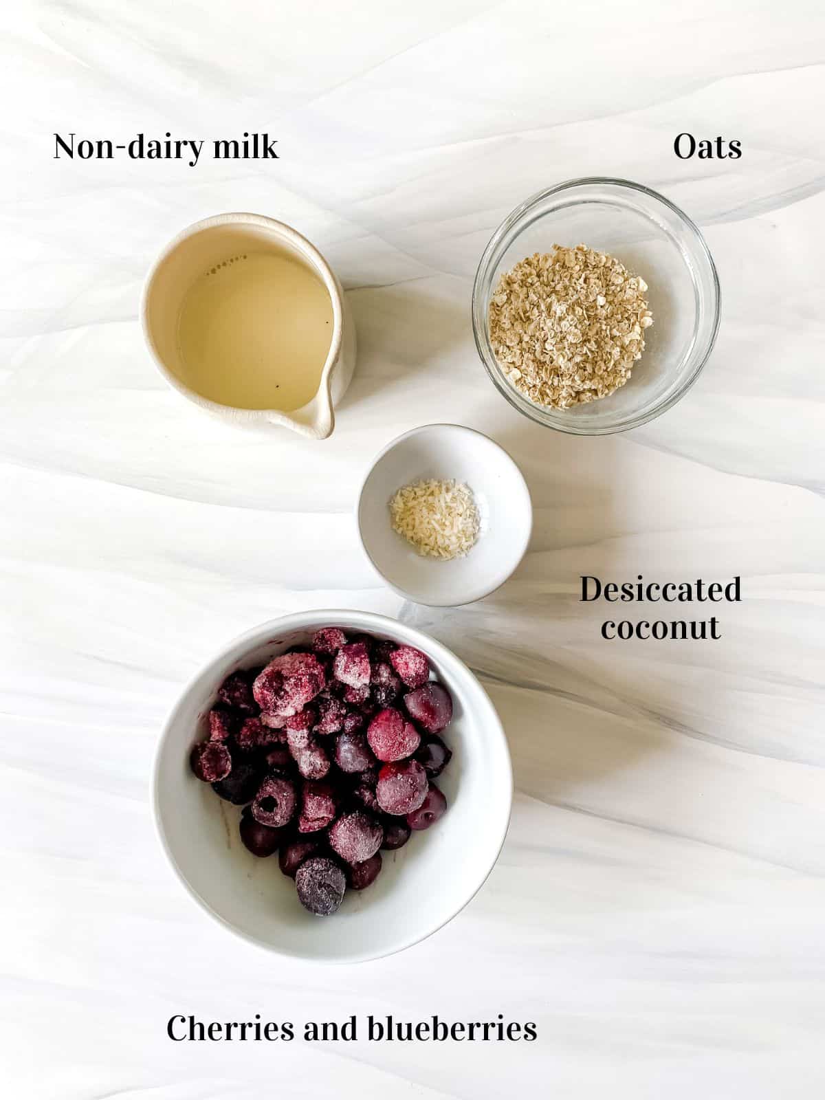 labelled ingredients to make cherry blueberry smoothie including a jug of milk and a bowl of fruit.