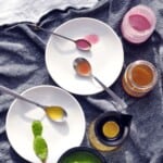 four salad dressings on spoons on two white plates on a dark blue cloth.
