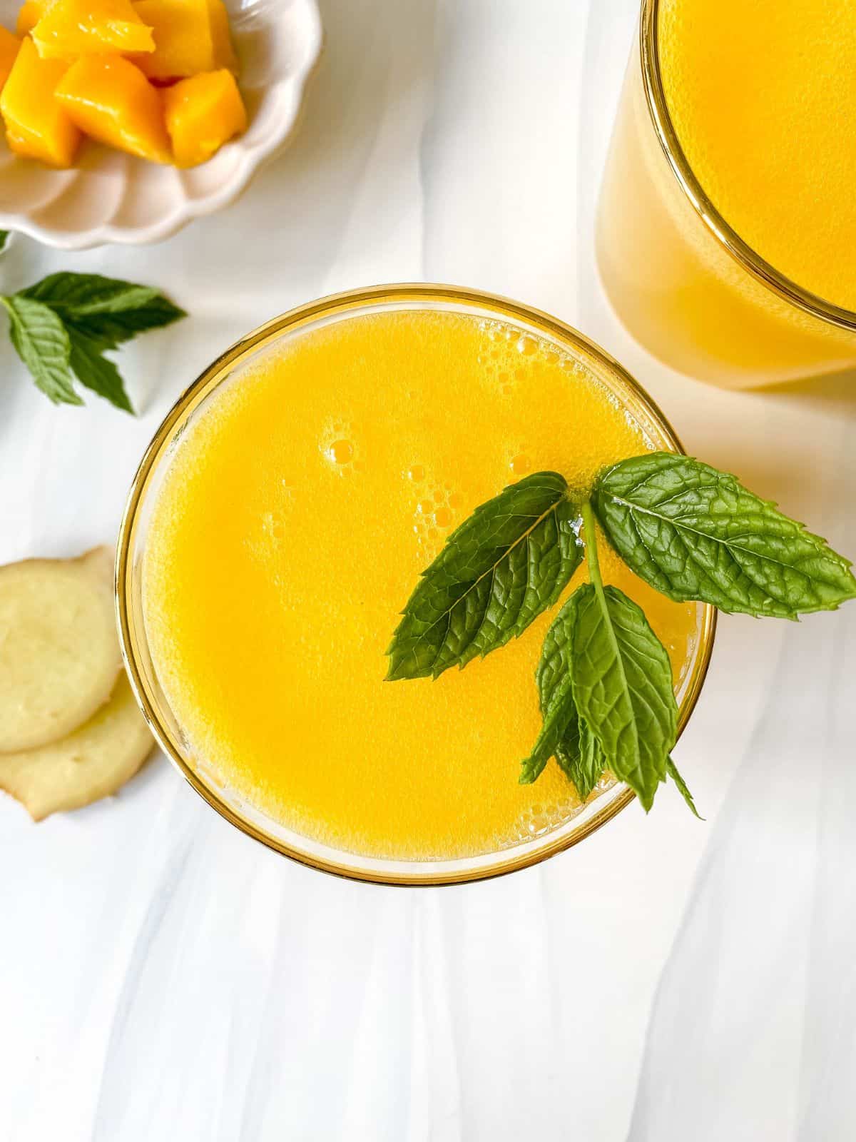 mango ginger mocktail in two glasses topped with mint next to a bowl of mango pieces.