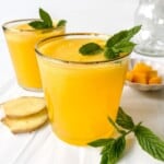 two glasses of mango ginger mocktail garnished with mint leaves with a glass pitcher in the background.
