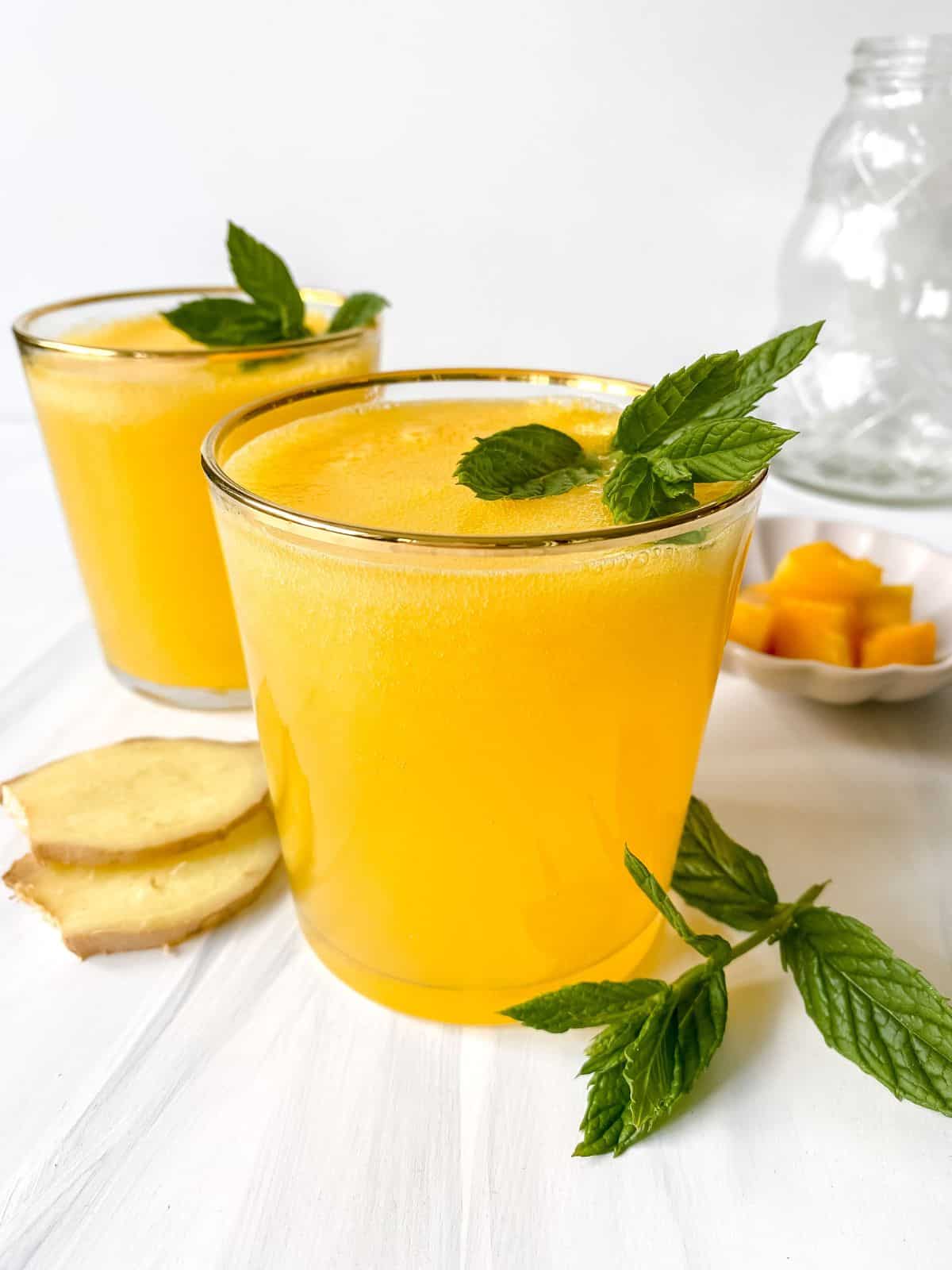 two glasses of mango ginger mocktail garnsihed with mint with a bowl of mango in the backgroud.