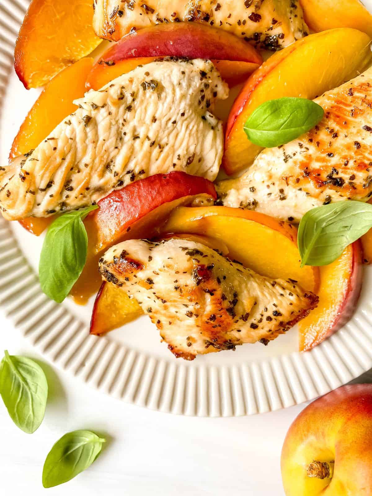 nectarine chicken on a cream fluted plate next to a nectarine and basil leaves.