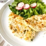 panko chicken breasts on a white plate with salad leaves and radish.