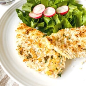 panko chicken breasts on a white plate with salad leaves and radish.