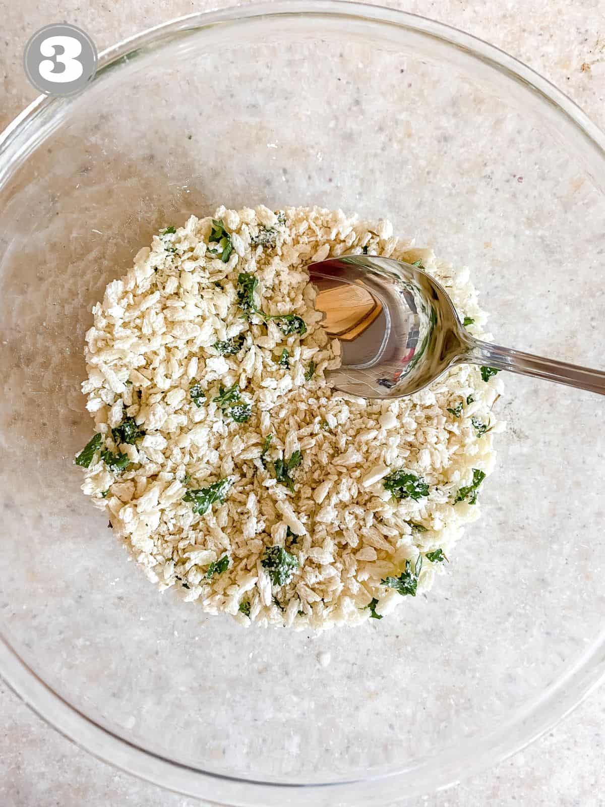 panko breadcrumbs and herbs being stirred by a spoon in a glass bowl.