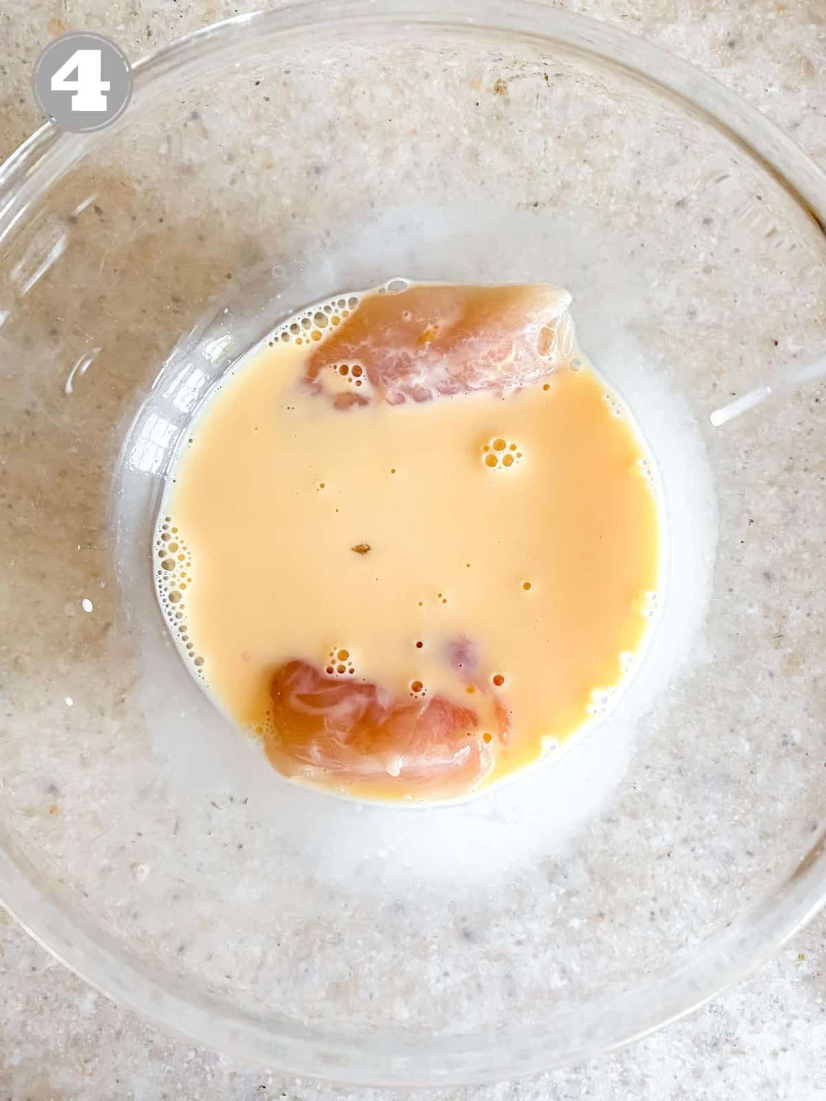 chicken breast in egg wash in a glass bowl.