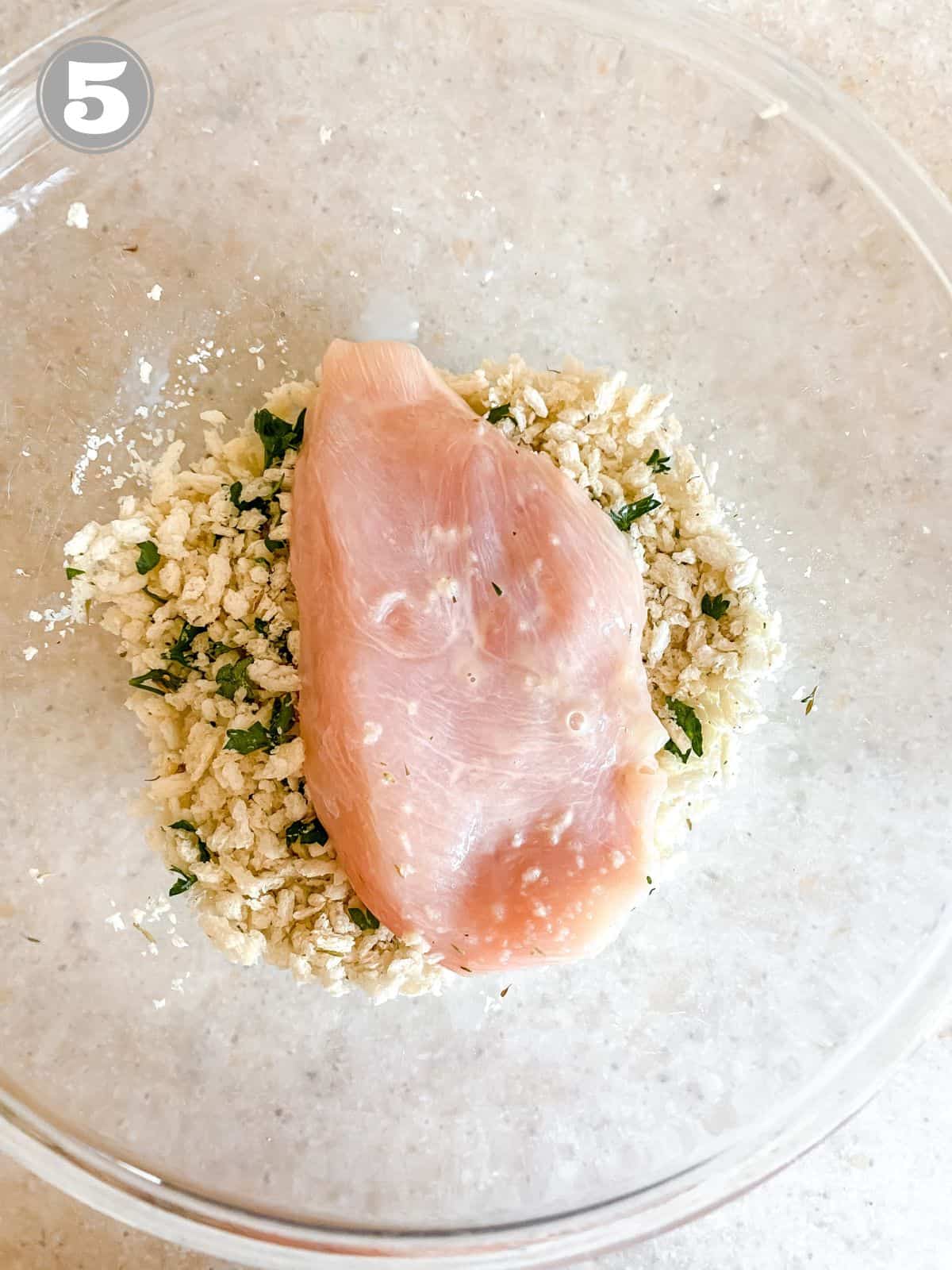 chicken breasts being coated in panko in a glass bowl.