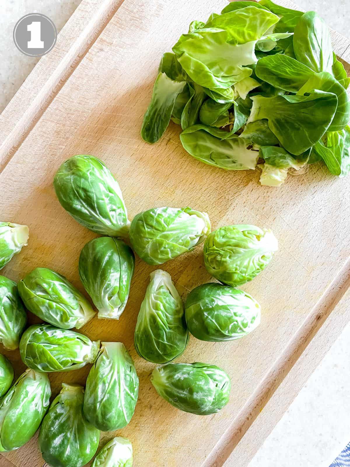 peeled Brussels sprouts next to sprout leaves on a wooden board labelled number one.