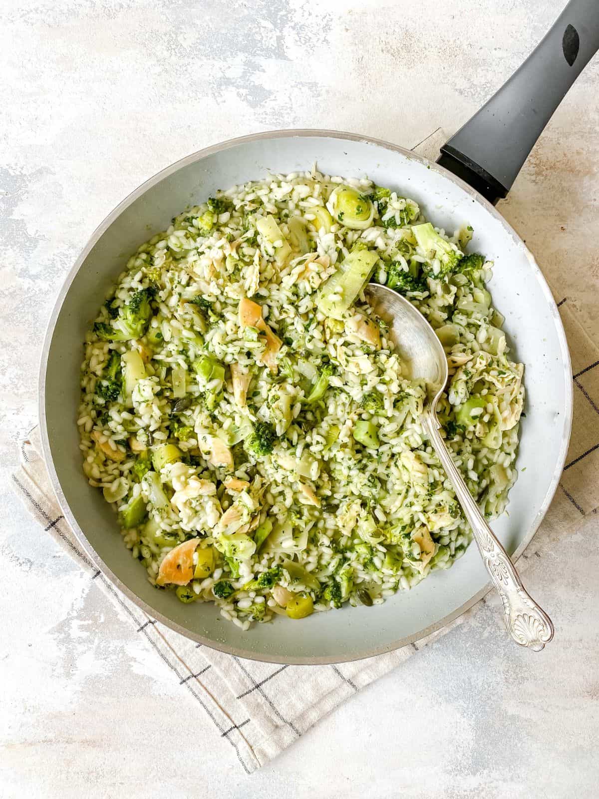pesto chicken risotto in a light grey skillet on a checked cloth.