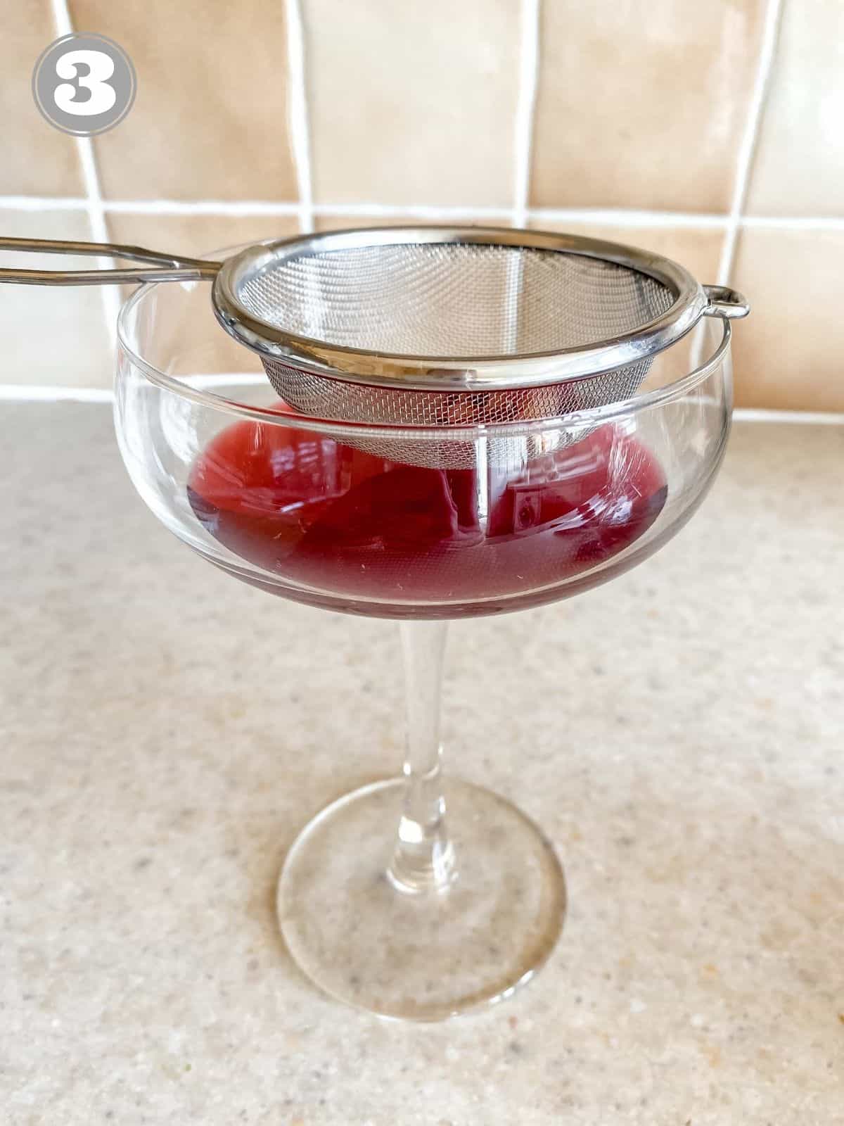 cocktail glass with pomegranate juice in it with a strainer on top.