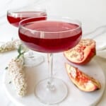 two glasses of pomegranate ginger mocktail on a marble tray next to white flowers and pomegranate.