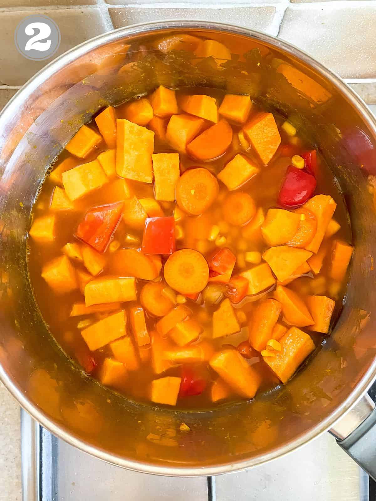 sweet potato, carrot, corn and bell pepper in broth in a pot.