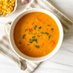 sweet potato corn chowder in a white bowl on a beige striped cloth next to a spoon and bowl of corn.