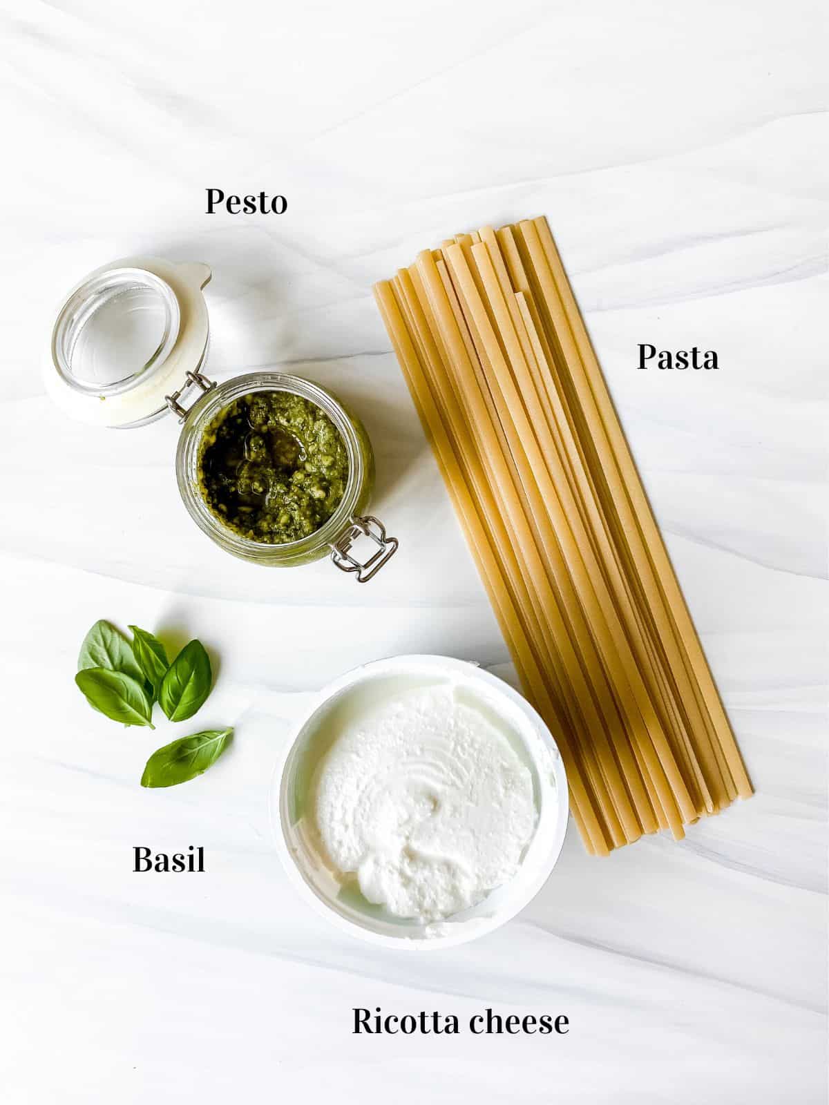 individually labelled pasta, a glass jar of pesto, basil leaves and ricotta cheese.