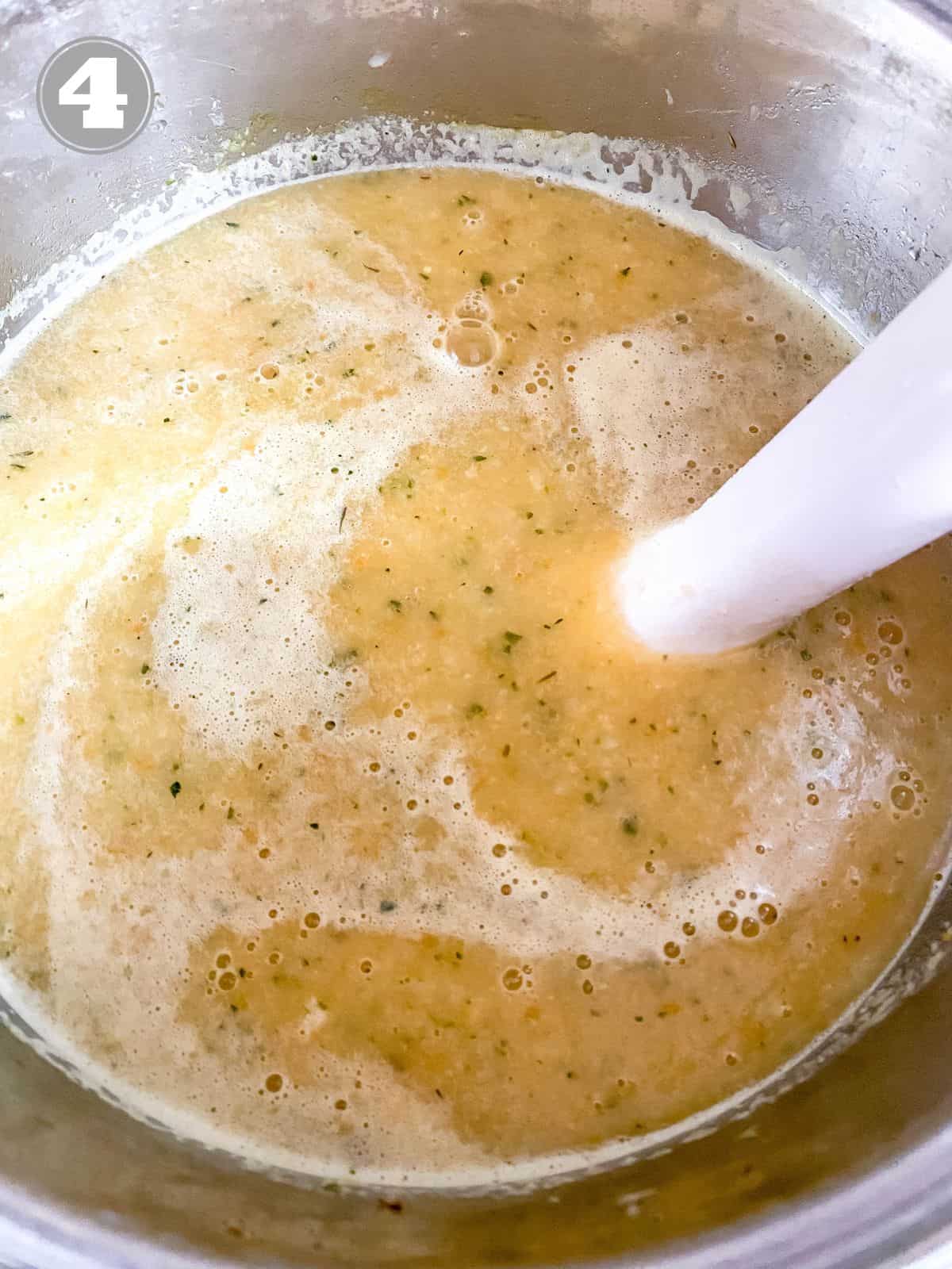 cauliflower zucchini soup in a pot being blended with an immersion blender labelled number four.