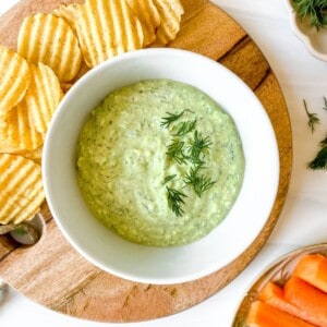 cottage cheese dill dip in a white bowl on a wooden board with chips.