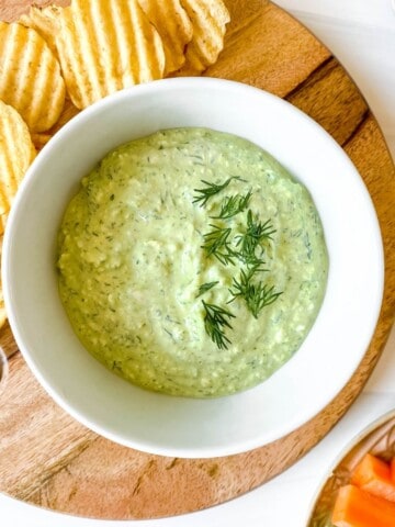 cottage cheese dill dip in a white bowl on a wooden board with chips.