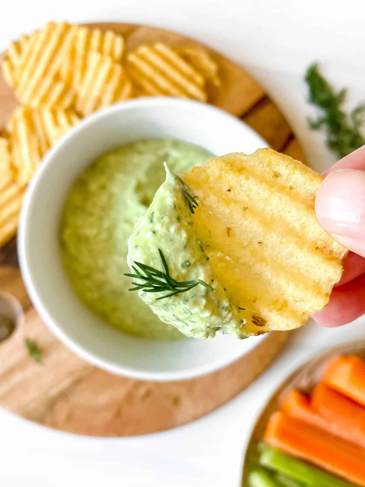 cottage cheese dill dip on a chip held in front of a white bowl of dip.