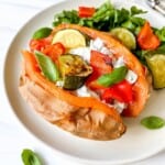 cream cheese stuffed sweet potato with roasted vegetables on a white plate with lettuce.
