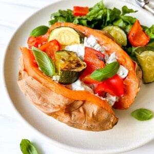 cream cheese stuffed sweet potato with roasted vegetables on a white plate with lettuce.