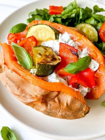 cream cheese stuffed sweet potato with roasted vegetables on a white plate with lettuce.