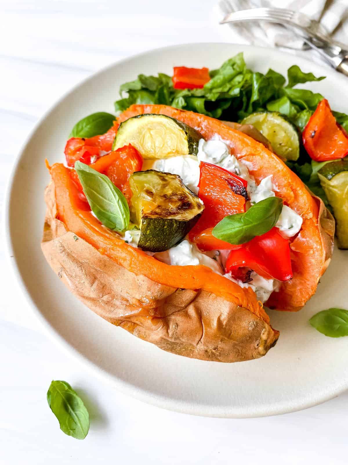 cream cheese stuffed sweet potato in a white plate with lettuce and roasted vegetables.