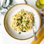 creamy zucchini linguine in a light grey bowl with a brown rim next to linguine, olive oil and garlic.