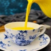 golden milk being poured out of a jug into a blue and white floral cup.