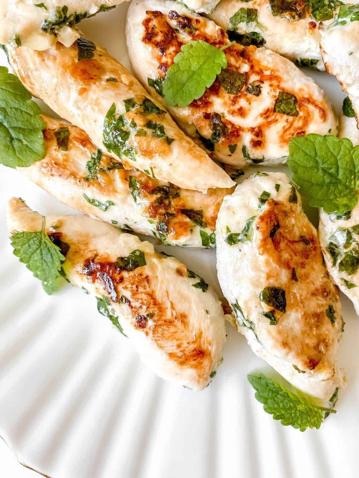 lemon balm chicken fillets on a white plate with fresh lemon balm leaves.