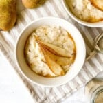 two cream bowls of pear porridge on a striped beige cloth next to a spoon and pears.