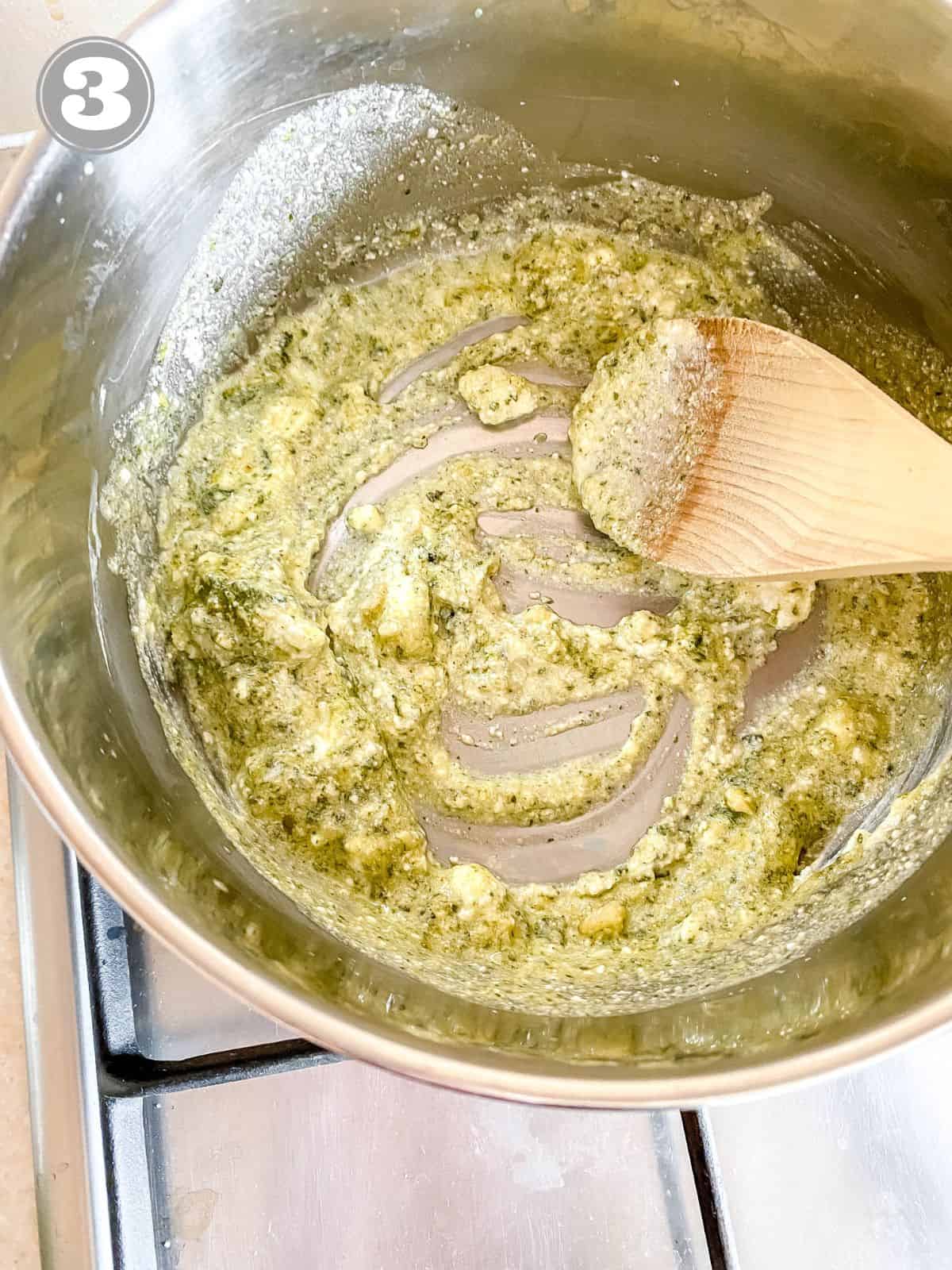 pesto ricotta sauce in a pot being stirred with a wooden spoon labelled number three.