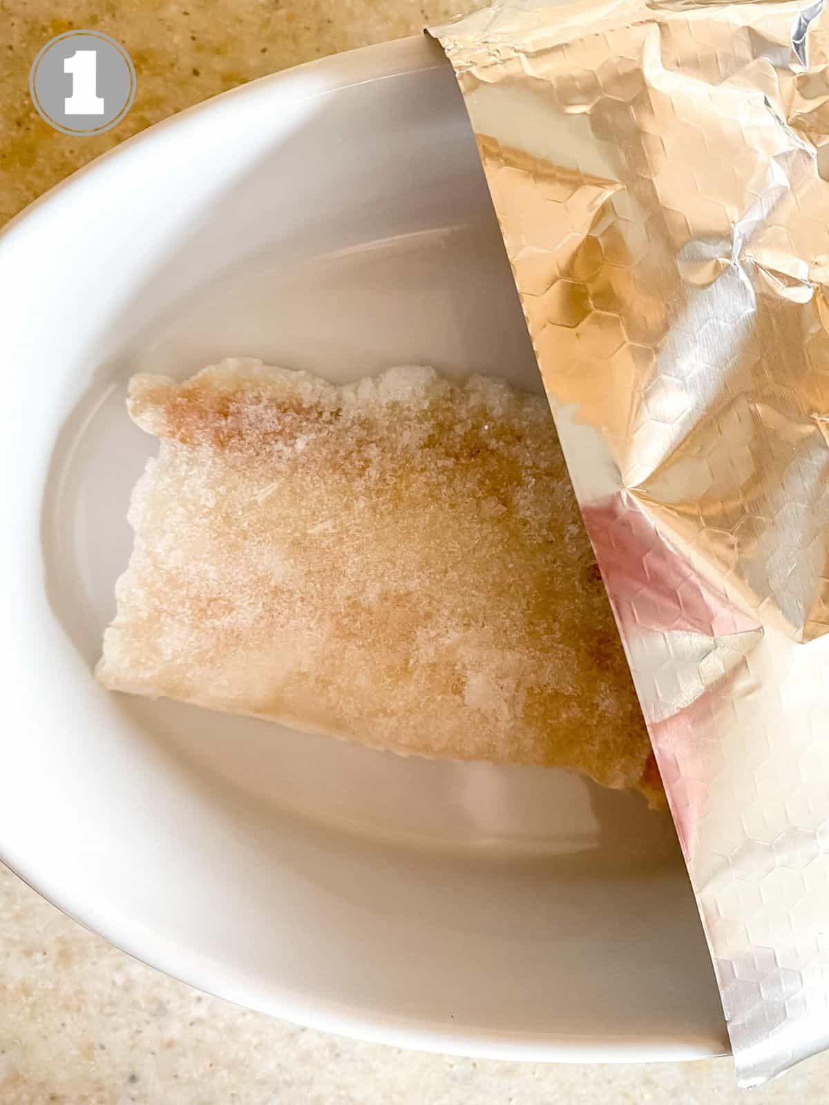 frozen cod in a white dish covered with aluminium foil.