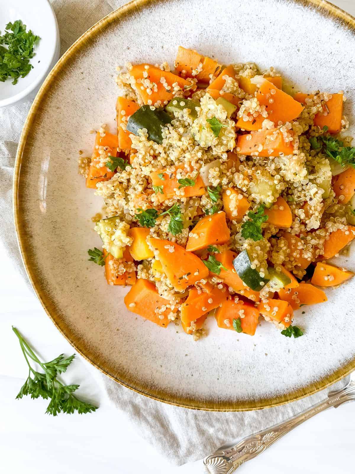 quinoa sweet potato bowl in a light grey bowl on a cloth with fresh herbs and a spoon.