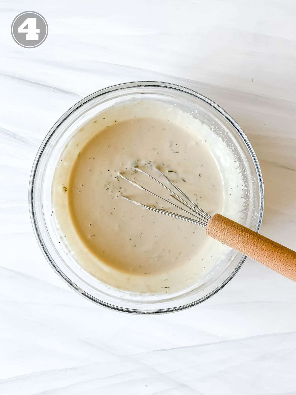 tahini dill dressing being whisked in a glass bowl numbered four.