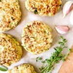 turkey rissoles on parchment paper on a wooden board next to garlic cloves and fresh herbs.