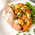 turkey stuffed sweet potato on a white plate next to arugula with a jar of tahini in the background.