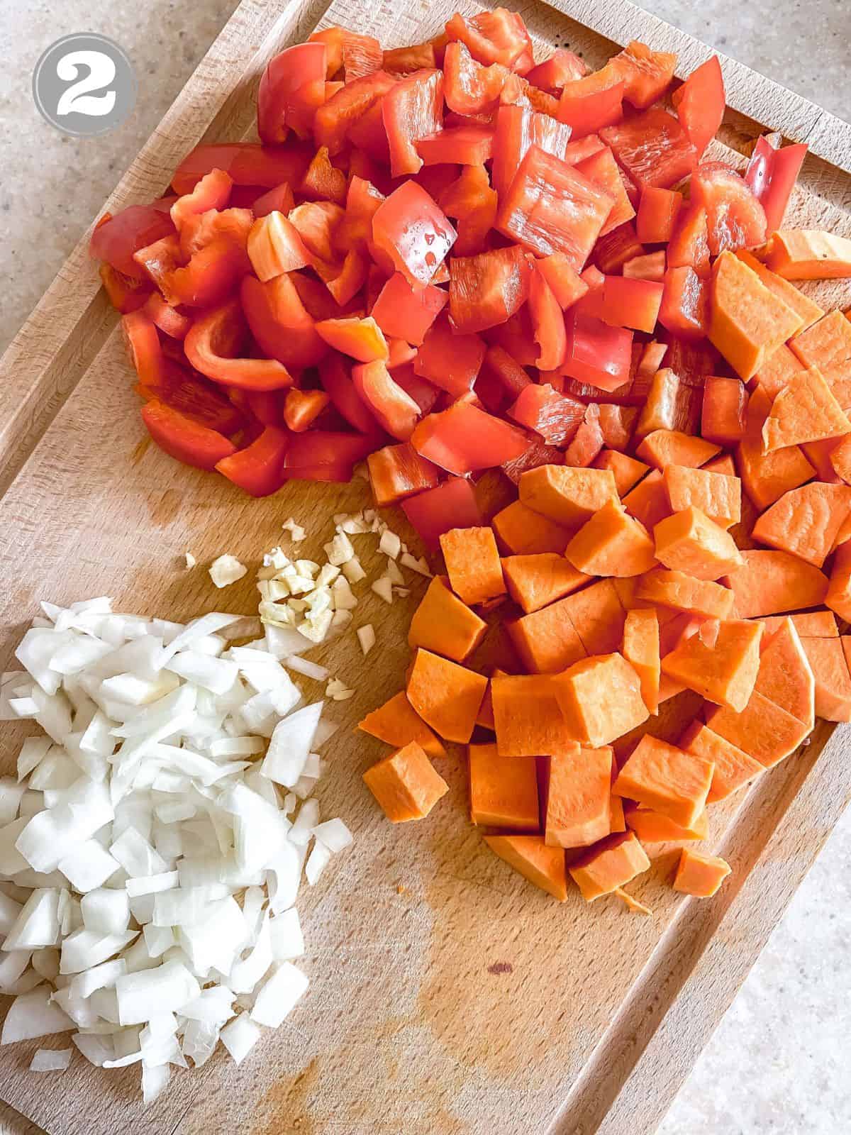 diced onion, garlic, bell pepper and sweet potato on a wooden board labelled number two.