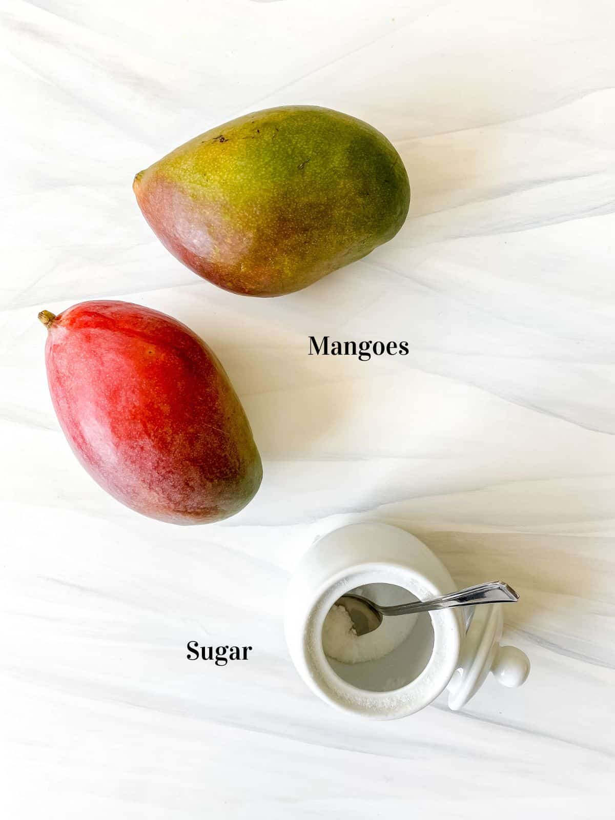 labelled mangoes and a white bowl of sugar with a spoon in it.
