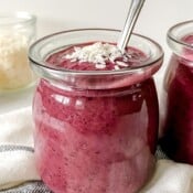 cherry chia pudding in two glass jars with a glass jar of coconut flakes in the background.