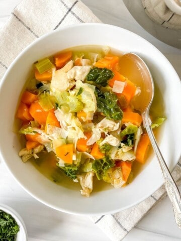 chicken and cabbage soup in a white bowl with a spoon in it on a beige checked cloth.