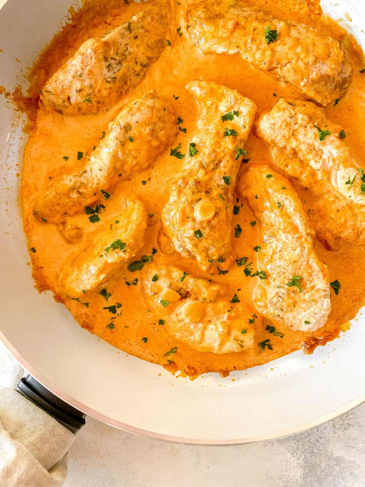 creamy paprika chicken in a light grey skillet with a cloth around the handle.