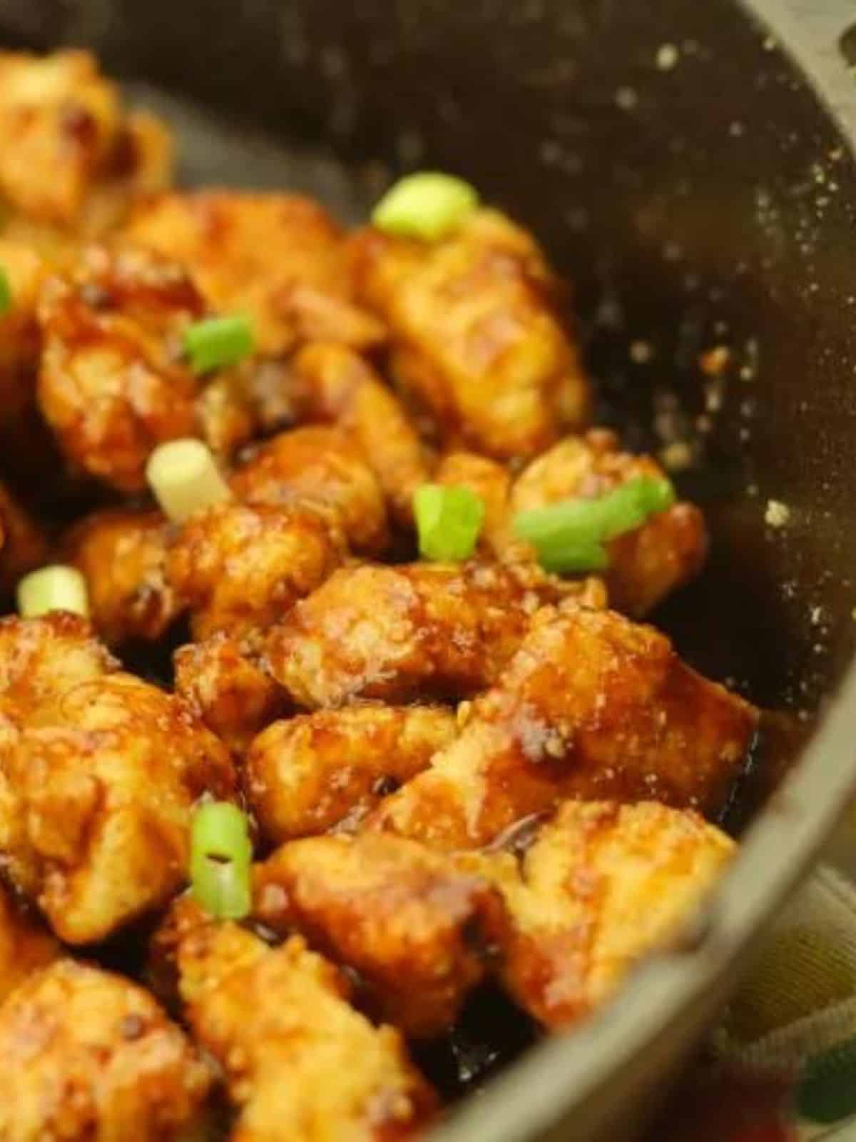 honey BBQ popcorn chicken garnished with green onion in a black cast iron pan.
