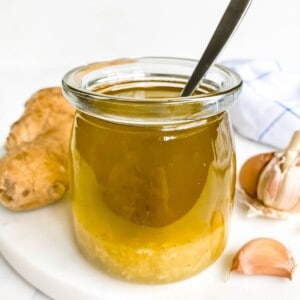 honey ginger salad dressing in a glass jar with a spoon in it next to garlic cloves.