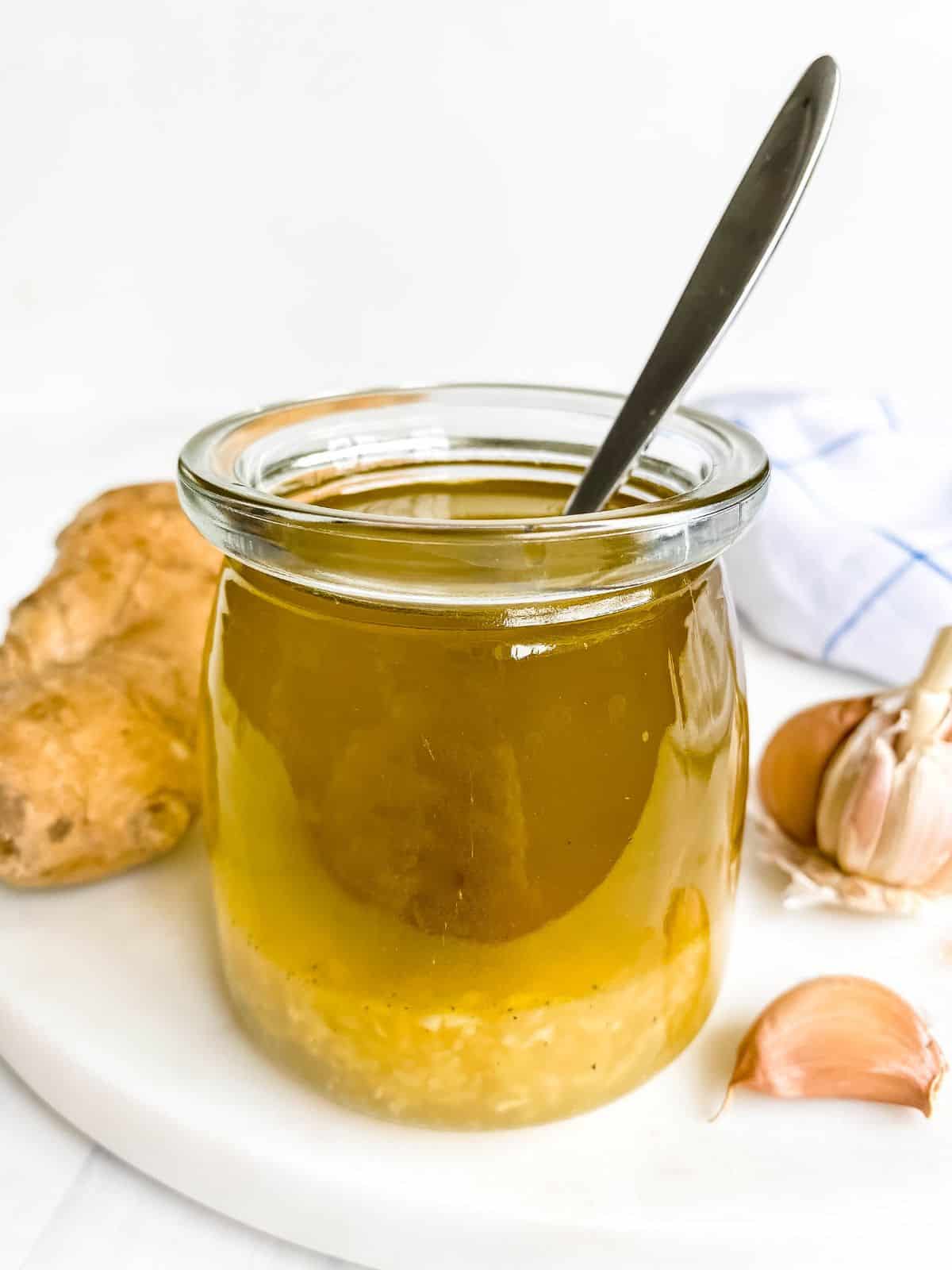honey ginger salad dressing in a glass jar with a spoon in it next to garlic and ginger.