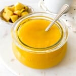 mango coulis in a glass bowl with a spoon in it with a bowl of mango cubes in the background.