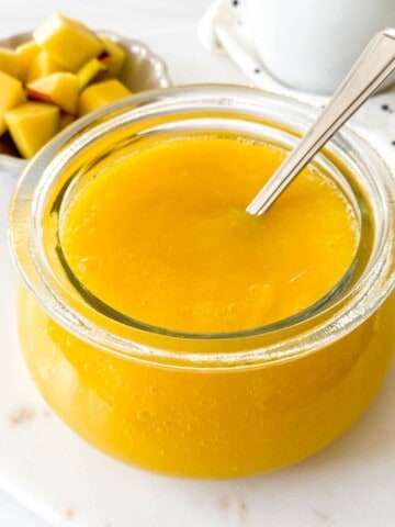 mango coulis in a glass bowl with a spoon in it with a bowl of mango cubes in the background.